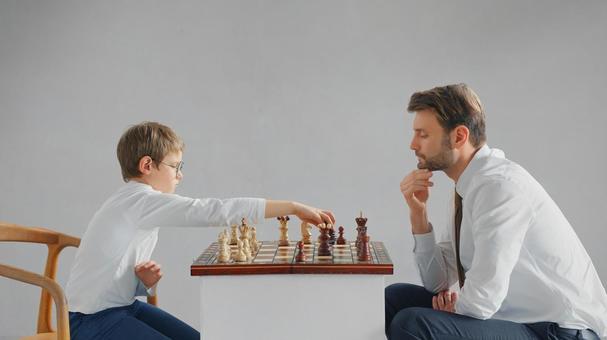 向かい合ってチェスをしている横向きの親子(グレー背景) 向かい合ってチェスをしている横向きの親子(グレー背景) チェス,親子,お父さんの写真素材