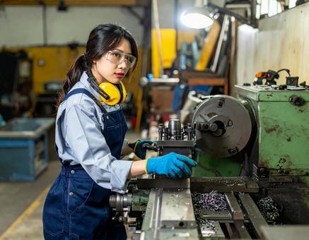 工場で加工機械で金属加工する女性スタッフ 工場で加工機械で金属加工する女性スタッフの写真