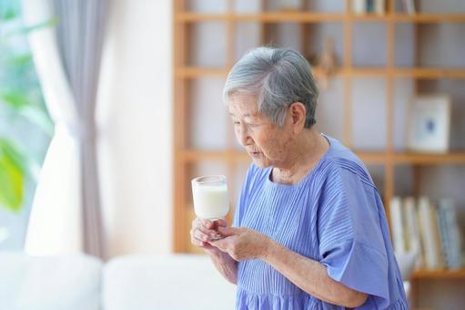 牛乳の入ったコップを見つめる高齢女性の写真