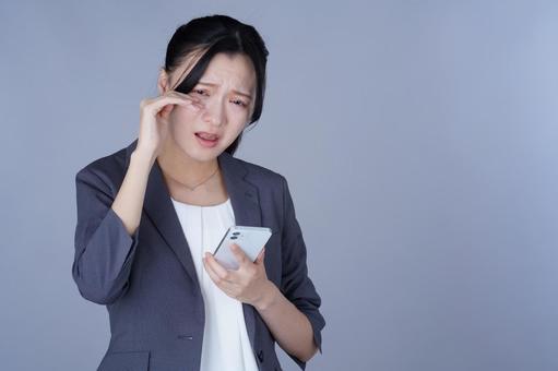 スマホを見て泣き顔のスーツ姿の女性の写真