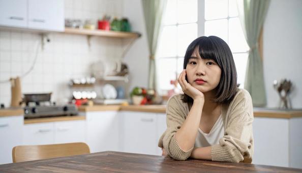 疲れた表情でキッチンに座る若い女性 疲れた表情でキッチンに座る若い女性の写真