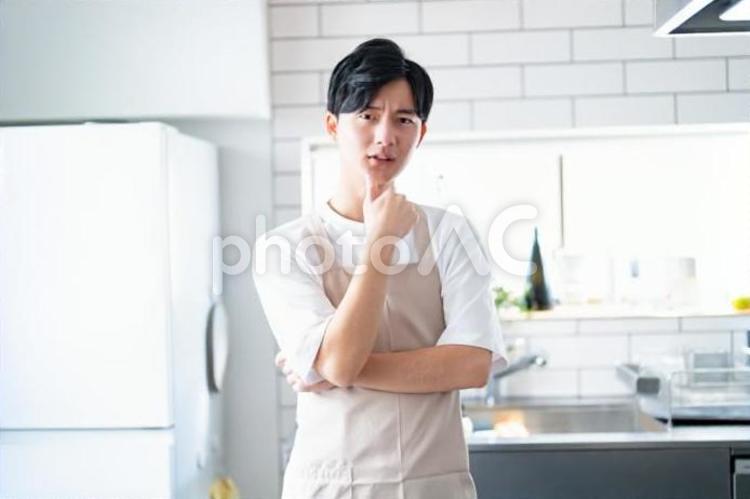 考えるキッチンでエプロンをつけた若い男性　 男性,料理,クッキングの写真素材