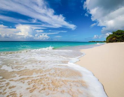 波が打ち寄せる砂浜。青い海と青空と雲。の写真