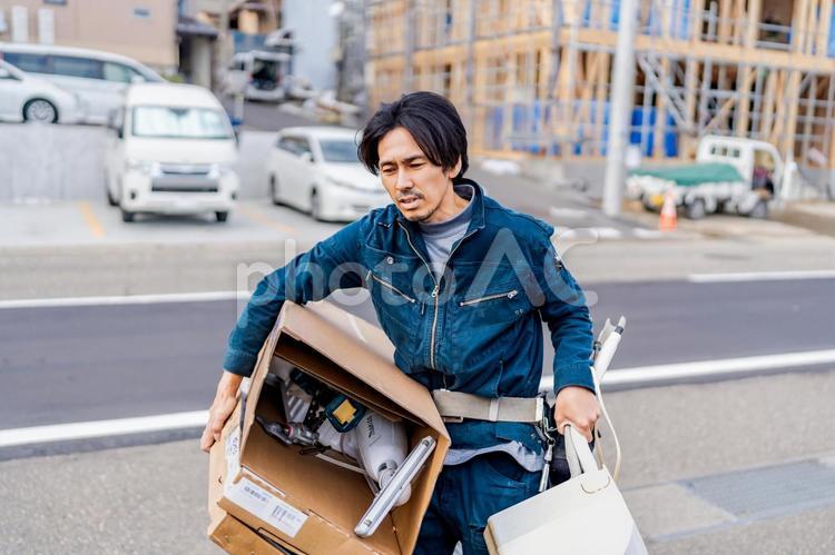 重そうに荷物を運ぶ電気工事作業員の男性 作業員,ビジネスマン,男性の写真素材