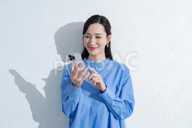 携帯を触る青いワンピースを着た女性 スマートフォン,スマホ,女性の写真素材