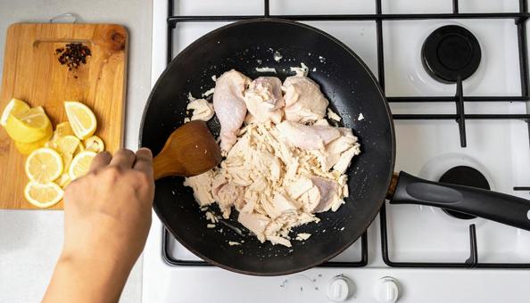 フライパンで鶏肉を炒める女性の手 フライパンで鶏肉を炒める女性の手の写真