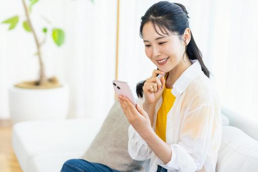 部屋でスマホを操作する女性 スマホ,笑顔,部屋の写真素材