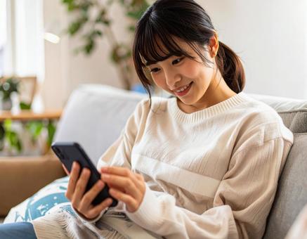 自宅のリビングでスマホを操作する女性 自宅のリビングでスマホを操作する女性の写真