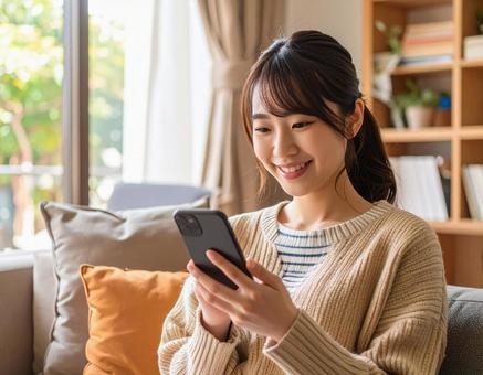 自宅のリビングでスマホを操作する女性の写真