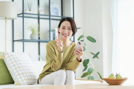 リビングでスマホを使うミドルの女性 スマートフォン,指さし,笑顔の写真素材