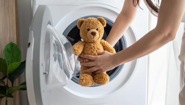 クマのぬいぐるみを洗濯機に入れる女性の手の写真