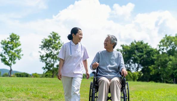 車椅子を押してシニア女性と笑う若い介護士 車椅子を押してシニア女性と笑う若い介護士の写真