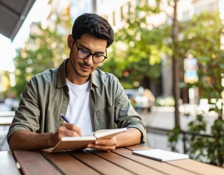 カフェでノートに書き込むメガネの男性 カフェでノートに書き込むメガネの男性の写真
