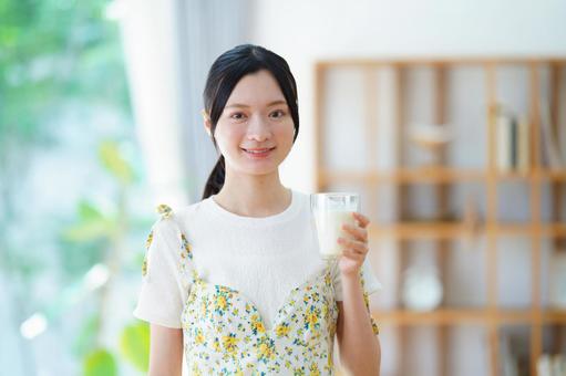 カメラ目線で牛乳を持ち微笑む半袖の女性の写真