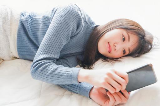 ベッドで寝る前にスマホを使う若い女性 スマートフォン,若い,休日の写真素材