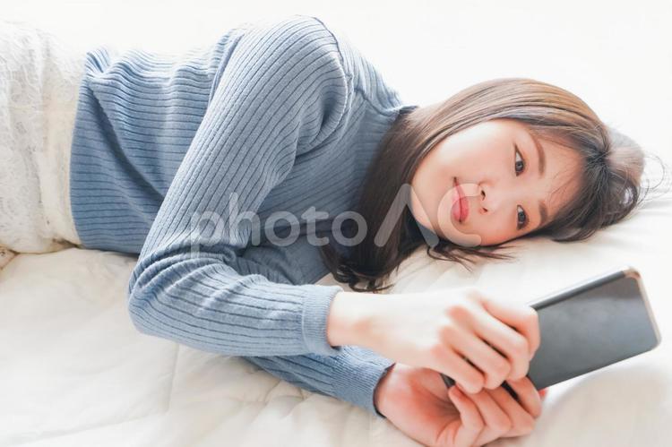 ベッドで寝る前にスマホを使う若い女性 スマートフォン,若い,休日の写真素材
