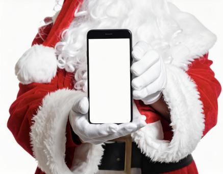 白いスマホの画面を見せるサンタクロースの写真