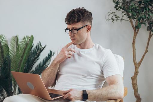 椅子に座って膝の上でノートパソコンを使うTシャツの男性 男性,外国人,欧米人の写真素材