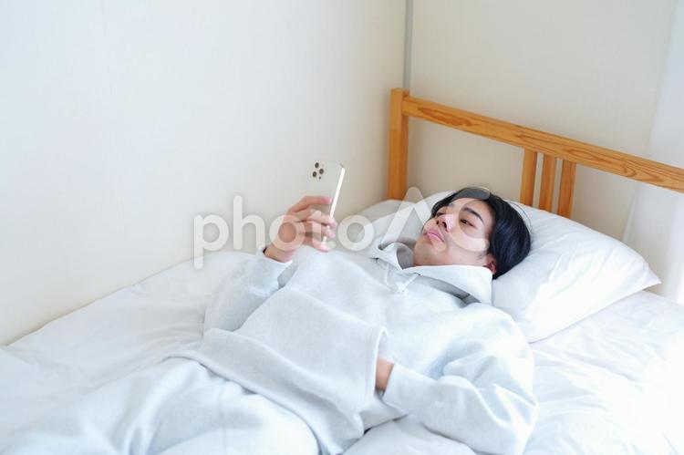 ベッドで寝ながらスマートフォンを見る男性 引っ越し,一人暮らし,男性の写真素材