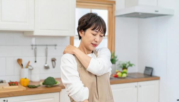 キッチンで肩こりを感じるエプロン姿の女性 キッチンで肩こりを感じるエプロン姿の女性の写真