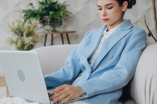 座ってノートパソコンで仕事する女性 女性,スーツ,水色の写真素材