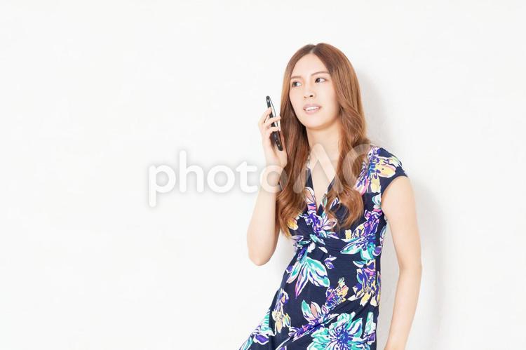 白い壁の前で、スマホを使う、青いワンピースを着た若い女性 女性,スマホ,携帯電話の写真素材