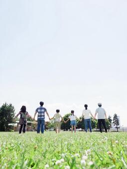A three-generation family holding hands in a sunny park A three-generation family holding hands in a sunny park