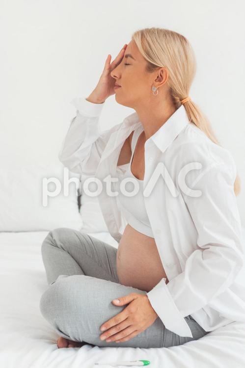 ベッドで頭を抑えておさえて目を瞑る女性 女性,人物,座るの写真素材