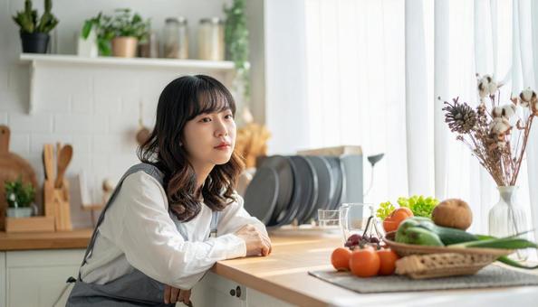 疲れた表情でキッチンに座る若い女性 疲れた表情でキッチンに座る若い女性の写真