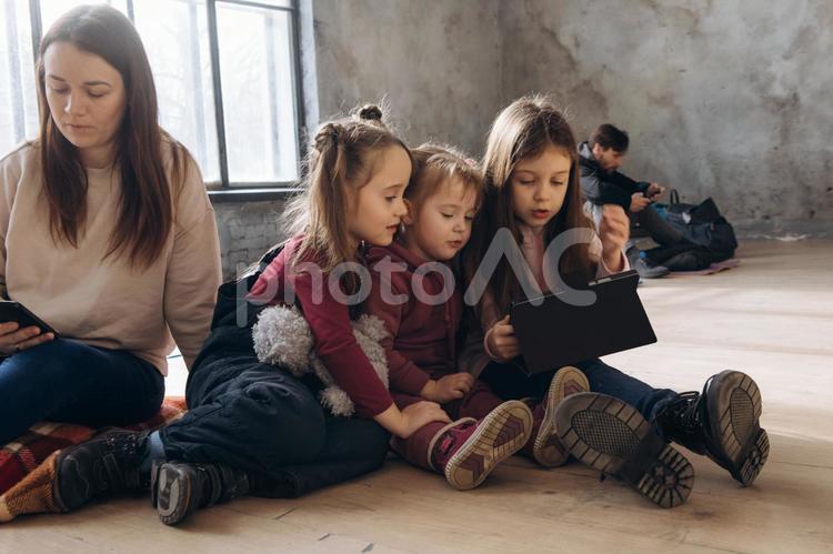 タブレットを見て携帯を見る女性と後ろにいる男性と子供たち 女性,女の子,人物の写真素材