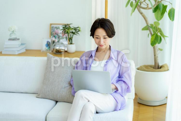 部屋でノートパソコンを使うミドル女性 女性,笑顔,テーブルの写真素材