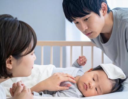 熱を出す赤ちゃんを心配そうに見守る夫婦の写真