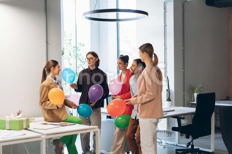 オフィスでみんなで風船を持って誕生日の女性を祝う ビジネス,ビジネスマン,ビジネスウーマンの写真素材