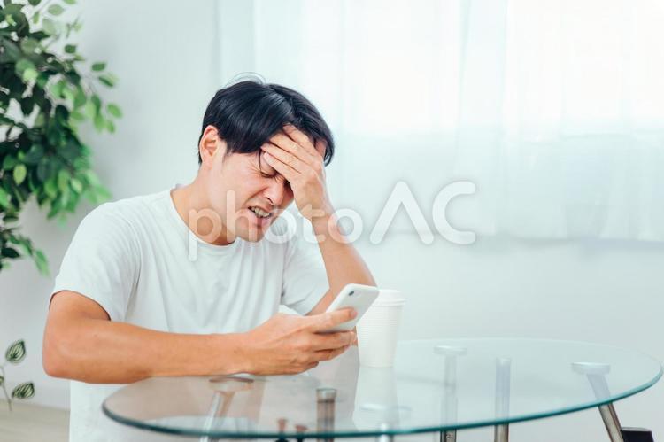 部屋でスマホを見る男性（悲しい） スマホ,スマートフォン,困るの写真素材