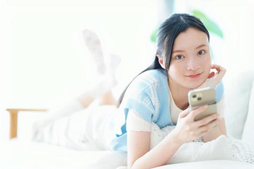 うつ伏せでスマホを持つカメラ目線の女性 女性,スマートフォン,持つの写真素材