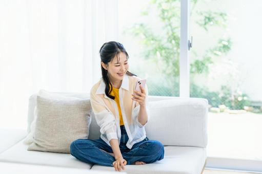 部屋でスマホを操作する女性 スマホ,笑顔,部屋の写真素材
