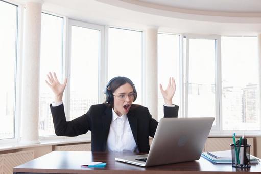 両手をあげパソコンを見るヘッドホンの女性の写真