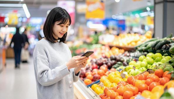 スーパーでスマホ決済を使う若い日本人女性 スーパーでスマホ決済を使う若い日本人女性の写真