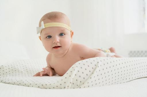 カメラ目線のリボンのヘアバンドをした赤ちゃん カメラ目線のリボンのヘアバンドをした赤ちゃん 赤ちゃん,腹ばい,うつ伏せの写真素材