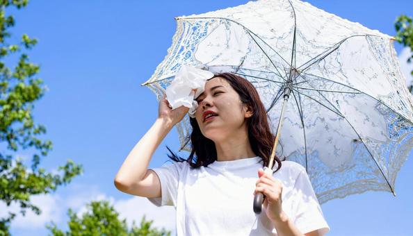 日傘をさして白いハンカチで汗を拭く女性 日傘をさして白いハンカチで汗を拭く女性の写真
