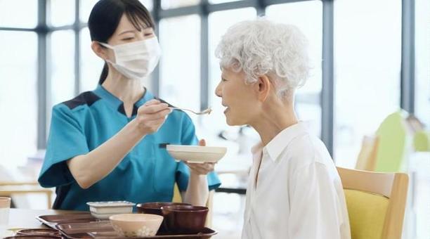 食事の介助をするアジア人介護士 食事の介助をするアジア人介護士の写真