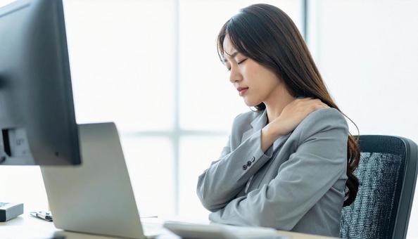 デスクワークで肩こりに悩むビジネスマンの写真