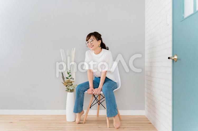 部屋で椅子に座るメガネをかけた日本人女性 メガネ,デニム,眼鏡の写真素材