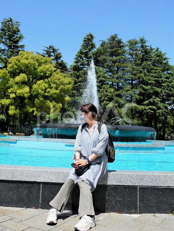 快晴の屋外で噴水と新緑の木々に癒される女性 女性,噴水,癒される女性の写真素材