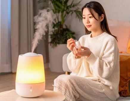 加湿器のそばでスキンケアをする女性 加湿器のそばでスキンケアをする女性の写真