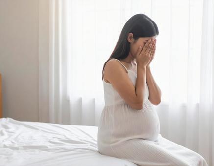 ベッドの上で泣いている妊婦 ベッドの上で泣いている妊婦の写真