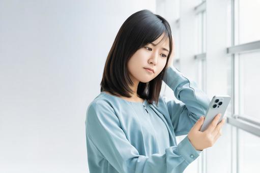 スマホを見て考える女性・ビジネスウーマン スマホを見て考える女性・ビジネスウーマンの写真