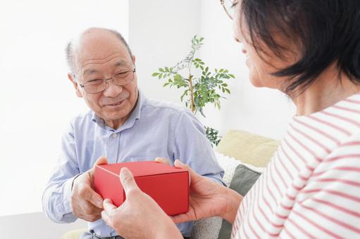 プレゼントを渡す高齢の夫婦 プレゼントを渡す高齢の夫婦 医療費,子供,貯金の写真素材