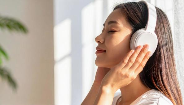 瞳を閉じてヘッドホンに手を添える女性 瞳を閉じてヘッドホンに手を添える女性の写真