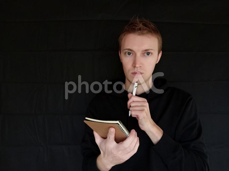 メモ帳をもって考えている男　外国人男性　黒バック メモ,仕事,メモするの写真素材